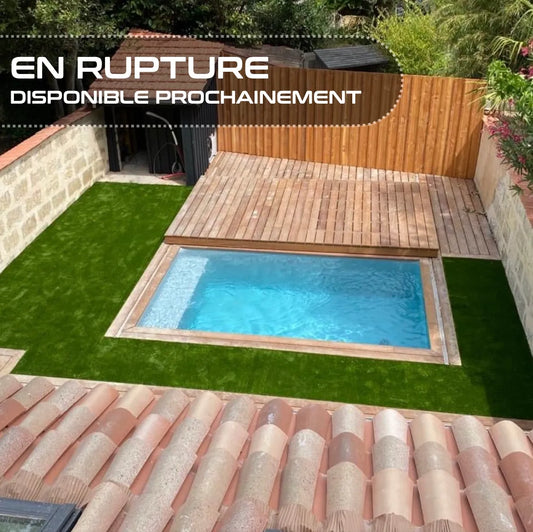 Vue d'une piscine entourée d'une terrasse en bois et d’une pelouse synthétique dans un petit jardin clôturé par des murs en pierre. Une bannière indique “EN RUPTURE - DISPONIBLE PROCHAINEMENT”.
